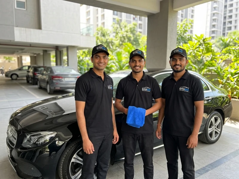 Three uniformed OTOGO car-care technicians standing beside a black luxury sedan